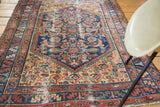 Distressed corner of antique Malayer rug, displaying blue, salmon, and yellow bordered patterns.