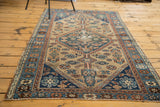 Distressed antique Hamadan rug corner with geometric motifs in indigo, sky blue, and terra cotta.