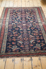 Distressed indigo field and red border of an antique Malayer rug, displaying playful herati motifs.