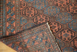 Folded corner of antique Belouch runner revealing hand-knotted weave and indigo, bronze gul motifs.