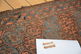 Angled detail: hand-knotted antique Belouch rug with indigo, bronze, and chestnut gul motifs.