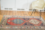 Distressed antique Northwest Persian rug fragment with brick red field, blue medallions, and ornate floral borders.