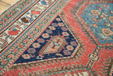 Distressed antique Persian rug fragment: intricate floral borders, deep blue medallion corner, brick red field.