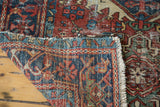 Distressed Persian Karaja rug's geometric patterns in brick red, navy, teal, and ivory, with fringe.
