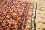 Bold geometric patterns in tiger orange, crimson, and charcoal on a vintage Caucasian rug.
