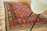 Secured corner of vintage Caucasian rug with crimson, tiger orange, and olive patterns.