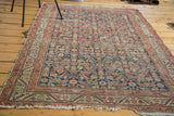 Distressed texture of a navy antique Malayer rug, showing Herati motif and Serbend border.