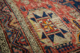 Distressed texture of a Caucasian Soumac rug, with geometric red, blue, and orange patterns.
