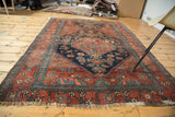 Distressed antique Persian Bijar rug corner, showcasing crimson red wool and deep blue tribal motifs.