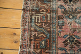 Distressed side of an antique Lilihan rug, featuring a brown border and faded raspberry field.