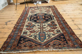 Distressed antique Hamadan rug corner, geometric floral motifs, indigo, terra cotta, ivory, and fringe.