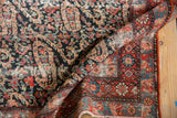 Distressed Malayer runner's curled edge, showing candy red border and dark blueberry paisley field.