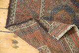 Distressed Antique Belouch rug corner with geometric pattern, secured dark brown side, and fringe.