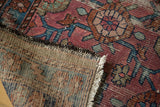 Distressed Antique Lilihan rug corner reveals faded fuchsia, blue pattern, and hand-knotted back.