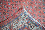 Folded corner of antique Mir Serbend rug reveals aged foundation and faded terra cotta blue field.