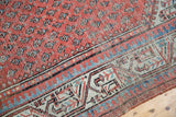 Faded terra cotta field with repeating blue boteh motifs and worn geometric border detail.