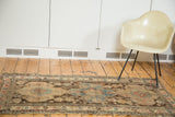 Distressed antique Caucasian rug with geometric patterns in muted sky blue, pink, and walnut brown.