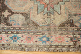 Close-up of distressed antique Caucasian rug, showing aged fringe and sky blue, pink geometric border.