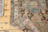 Distressed antique Caucasian rug corner, showing worn geometric patterns, blues, pinks, and hand-knotted weave.