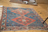 Distressed pile texture on a corner of the antique Persian rug, showing red medallion and blue geometric field.