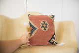 Hand holding a handmade Kilim pillow, showcasing its aged flatweave, faded red, blue, and tan geometric patterns.