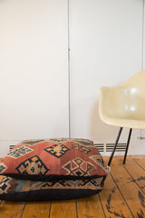 Two stacked antique Kilim floor pillows, displaying time-softened geometric patterns and black linen back.