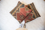 Two geometric antique Kilim floor pillows with faded colors, beside sneakers.