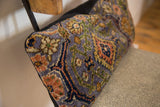Angled close-up of textured purple Bibikabad rug fragment pillow with orange and green motifs.