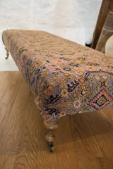 Turned wood leg with brass caster wheel of the vintage rug ottoman.