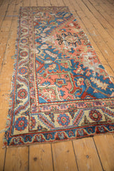 Tattered edge of antique Serapi rug, highlighting sapphire blue and coral geometric patterns.