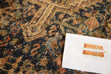 Decorative distressed pile of vintage Shiraz rug, in navy blue, blush, and coffee tones.