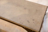 Rough soapstone surface with dark spots and aged metal edge of industrial table.