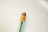 Close-up of the vintage peg doll's hand-painted face, black hair, and orange top.