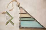 Detail of handmade stained glass art, showing opaque pastel pink, cream, green, and blue panels.