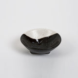 Modern handmade ring dish with black and speckled ecru glaze and three small legs.