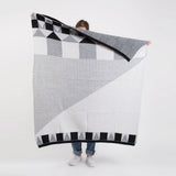Modern black, white, gray blanket with bold geometric blocks and stripes, held up.