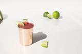 Shiny handmade Copper Cup with a reddish drink, garnished with lime and watermelon.