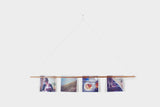 Simple copper plated steel photo bar hanging by a cord, displaying four pictures.