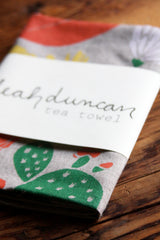 Folded Leah Duncan cactus tea towel on natural linen, green pattern and brand label.