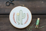 Handmade green cactus embroidery with yellow flower, rust branches on muslin in wood hoop.