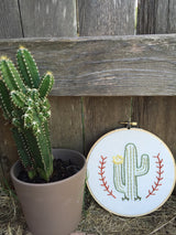Hand-stitched green cactus art with yellow flower, on a natural wood hoop.