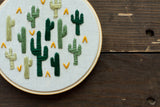 Textured green cactus embroidery with yellow accents on unbleached muslin.