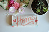 Natural unbleached cotton tea towel printed with coral pink 'Home' script and heart motifs.