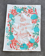 Natural cotton 'Our House is a Home' tea towel with a vibrant floral wreath.
