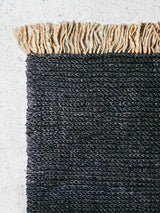 Dense, hand-woven charcoal hemp texture paired with a thick, natural fiber fringe.