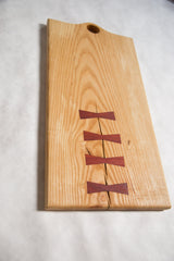 Hickory cutting board's natural wood crack mended with four reddish-brown butterfly inlays.