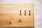 Maple cutting board with natural grain and dark bow-tie wood mends.