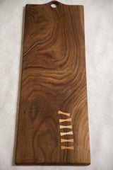 Rich walnut serving board featuring unique light bow-tie inlays and wood grain.