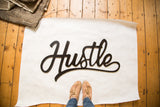 Black script 'Hustle' sign, cut from plywood, showing its hand-painted texture, 32 inches wide.