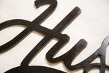 Hand-painted black plywood texture on the 'Hustle' sign, revealing wood grain.